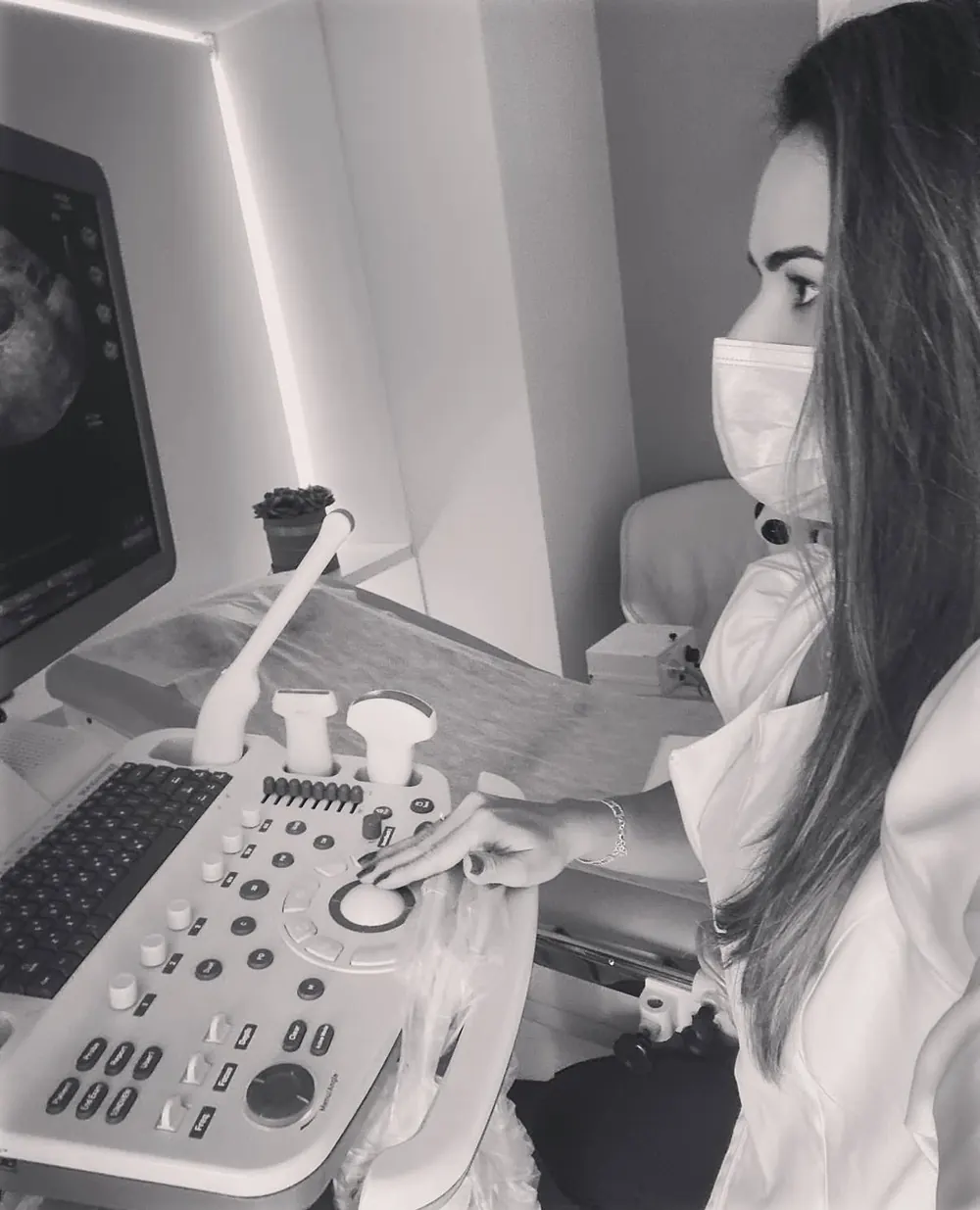 Dra. Sabrine Vilán, de máscara e jaleco, operando um aparelho de ultrassonografia